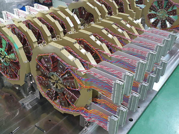 Multiple precision octupole magnets with complex wiring harnesses lined up on a worktable