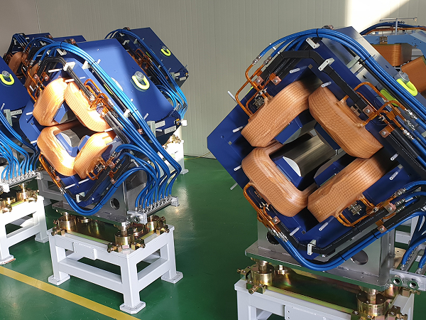 Technician inspecting yellow and blue quadrupole magnets in the factory