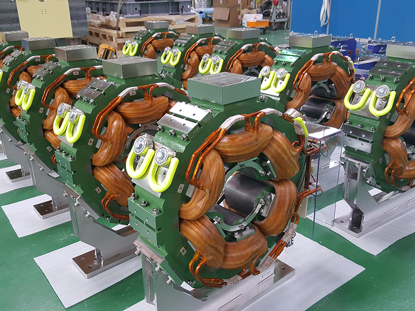 Row of green sextupole magnets with exposed copper coils in a factory